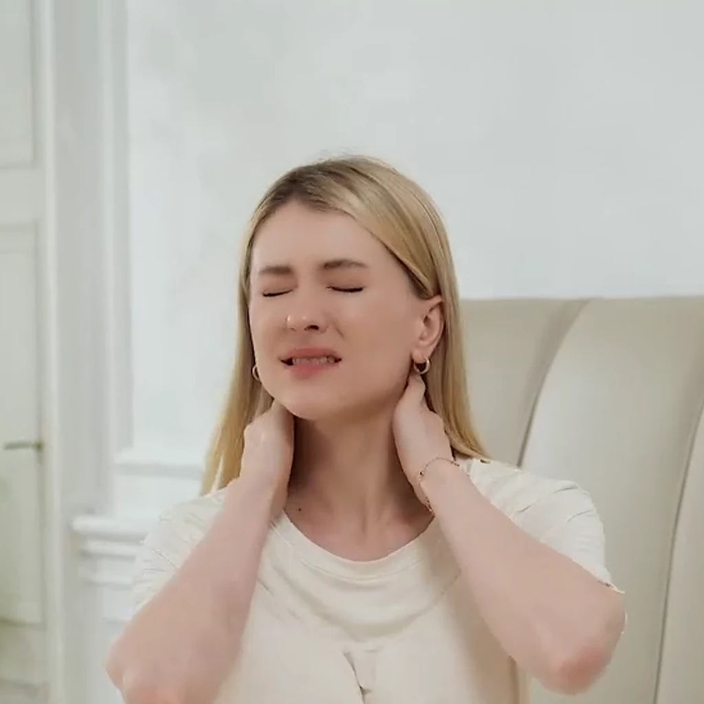 Femeie așezată pe pat, cu mâinile pe gât